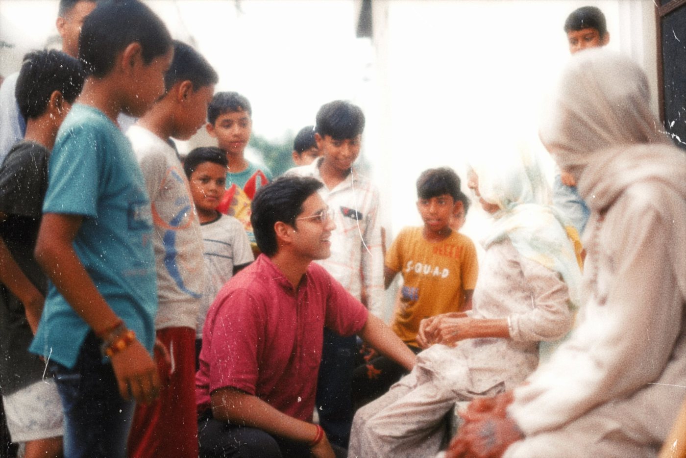 Sudhanshu crouched among village children, talking with elders